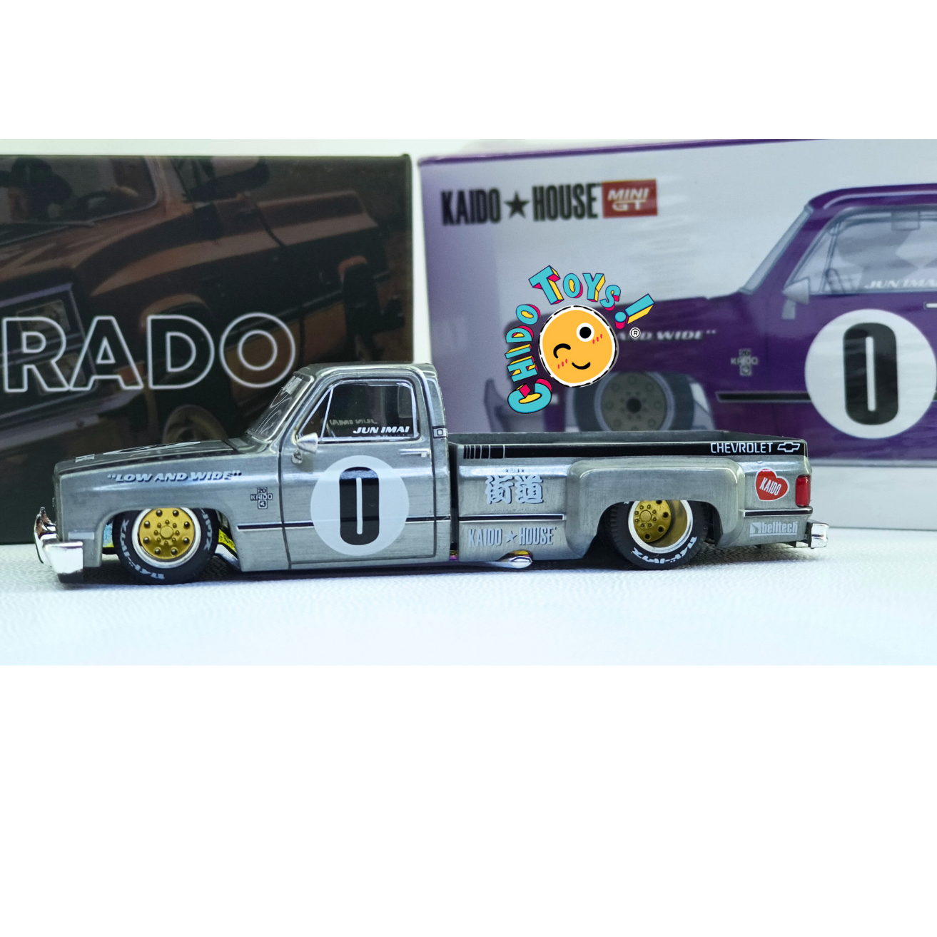 Kaido House Chevrolet Silverado CHASE 1:64 gris metálico con rines dorados, cofre abatible y llantas de goma