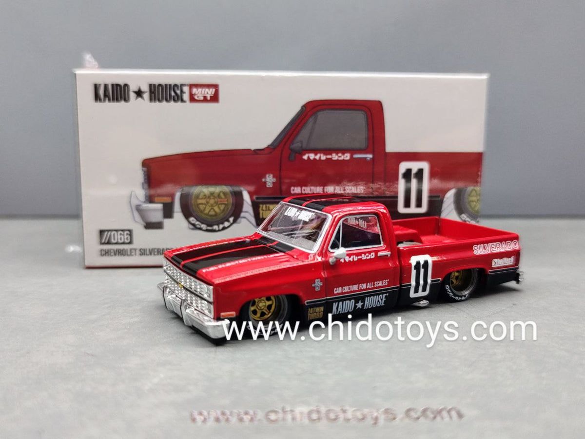 Kaido House Mini GT Chevrolet Silverado V1 1983 1:64 roja con franjas negras, rines dorados, cofre abatible y caja sellada.