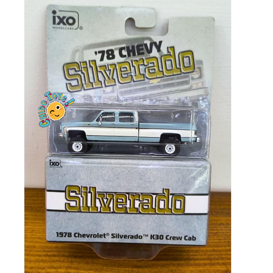 IXO Chevrolet Silverado K30 Crew Cab 1978 escala 1:64 azul claro y blanco con carrocería metálica, neumáticos todoterreno y blíster original.